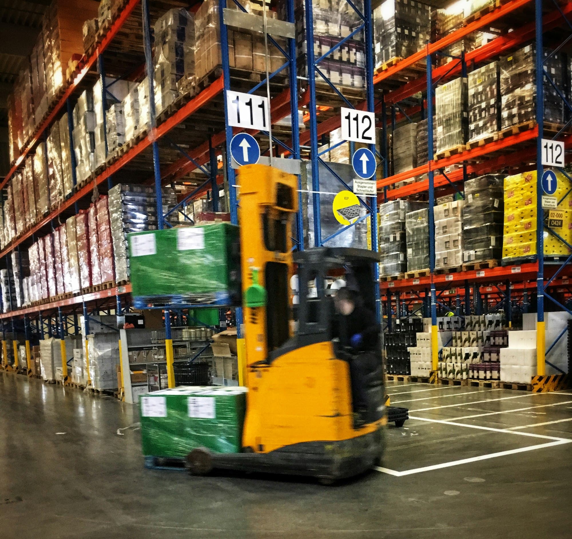 Un carrello elevatore in un corridoio di magazzino pieno di merce imballata